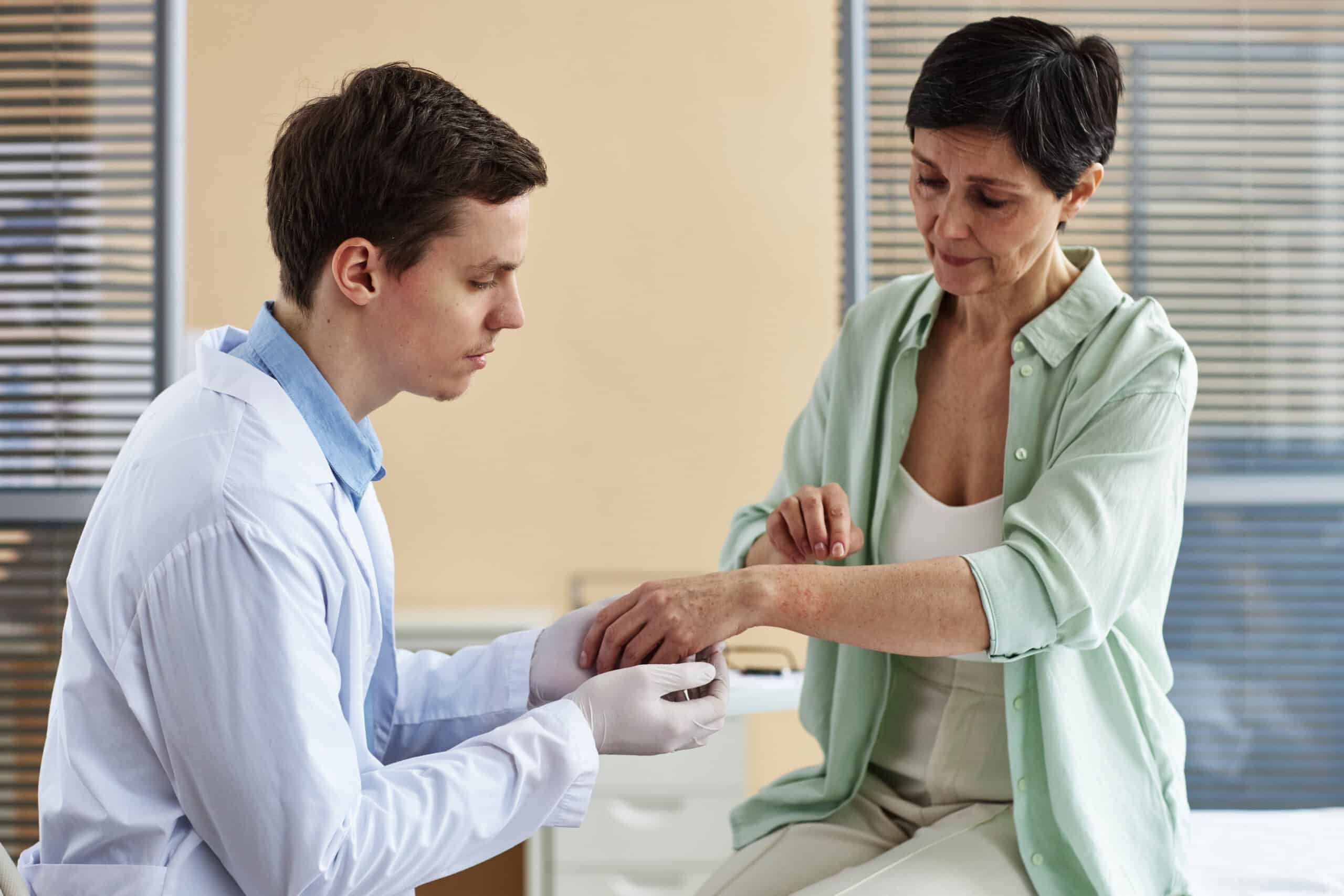 Side view portrait of doctor examining hands of mature woman during consultation in dermatology clinic, copy space